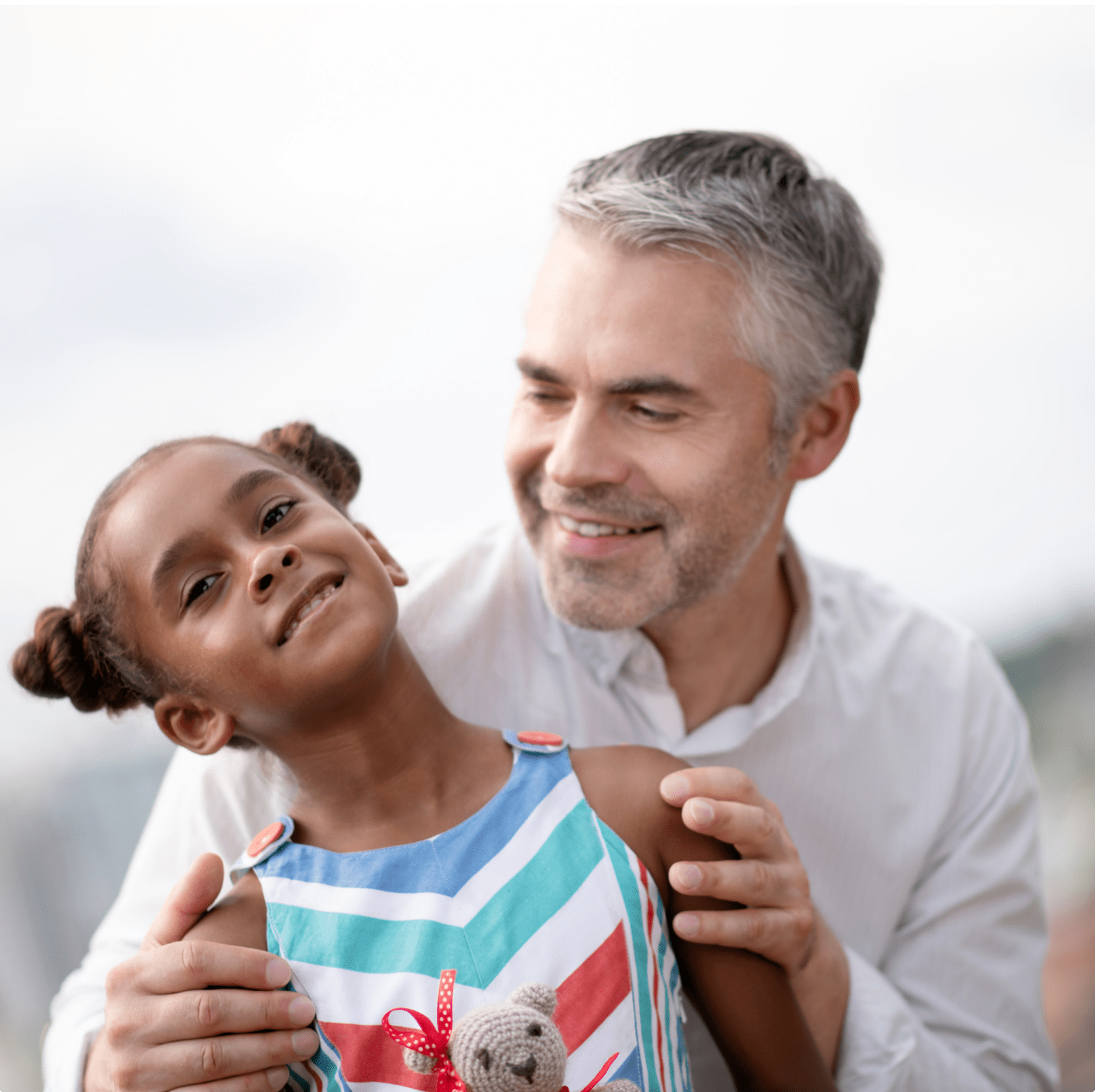 Child smiling at camera with head tilted with man behind her smiling at her.