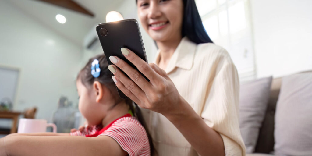 Woman holding a phone smiling with a child on her lap.