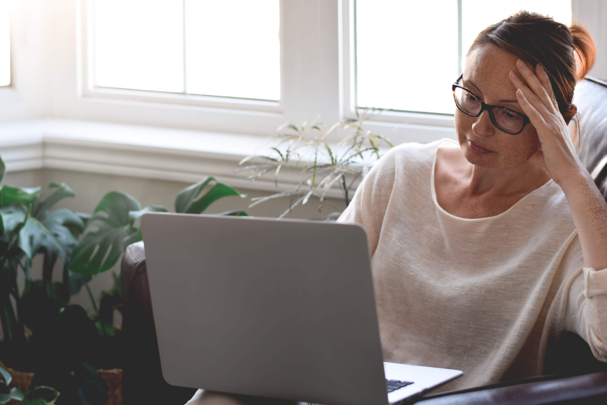 Someone sitting on a couch looking at a computer screen looking tired.