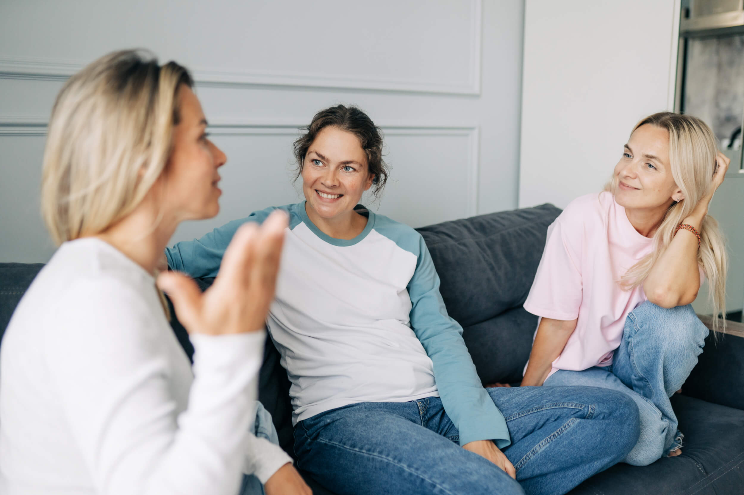 Three people sitting on a couch talking and smiling.